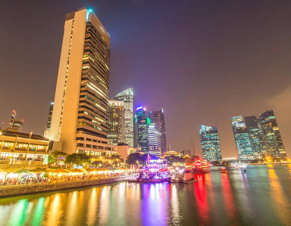 Clarke Quay’s riverside dining area at night with colorful lights reflecting on the water.