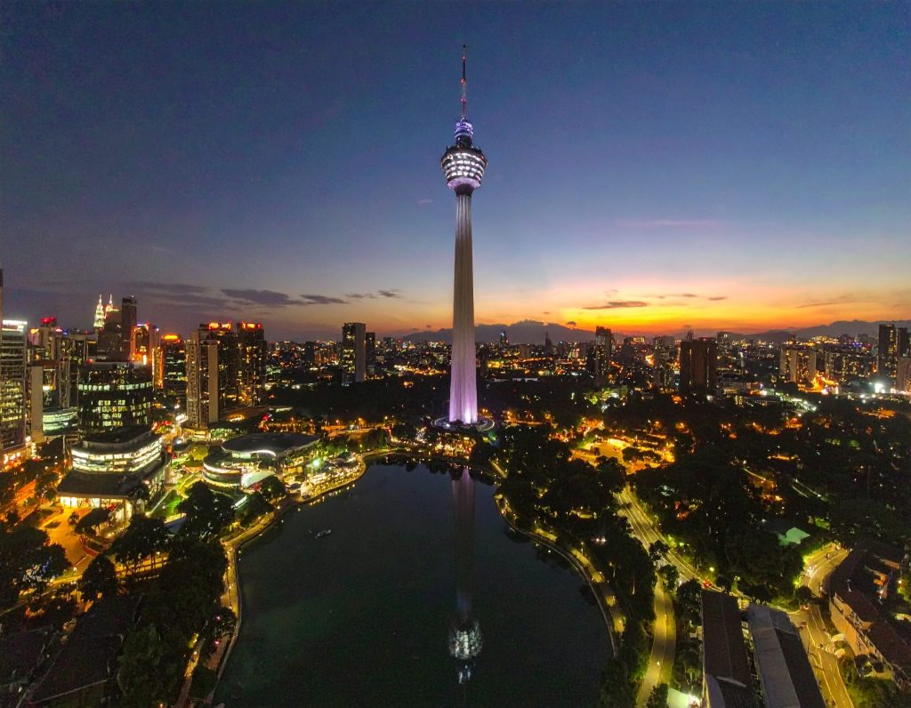 KL Tower rising above Kuala Lumpur city skyline on a sunny day.