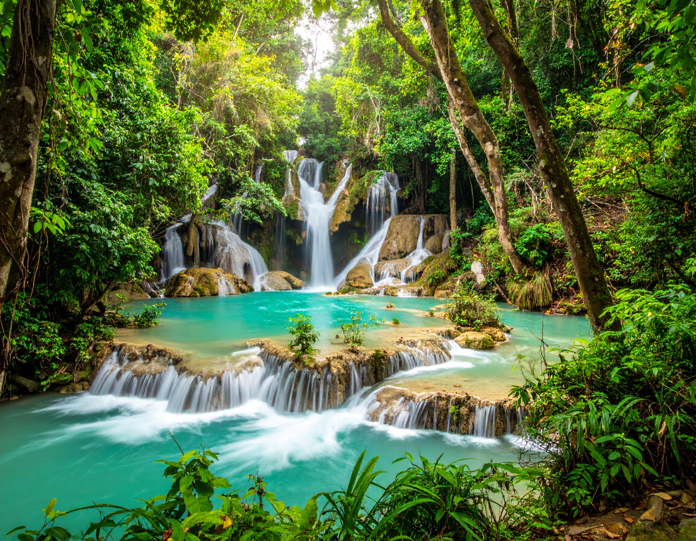 Turquoise cascading Kuang Si Falls surrounded by lush jungle in Laos